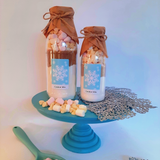 Two bottles of cookie mix with marshmallows on a blue stand, surrounded by decorative elements.
